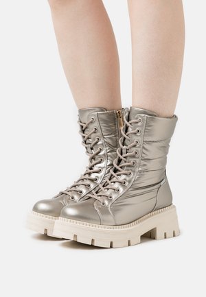 Metallische silberne Schnürstiefel mit gepolsterter Textur, einer klobigen weißen Sohle und einem seitlichen Reißverschluss für einfachen Zugang. Detaillierte Nähte an den Seiten.