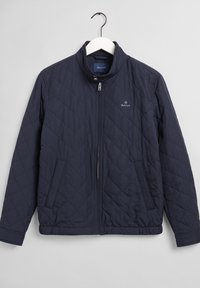Navy blue quilted jacket with front zipper, stand collar, two side pockets, and small GANT logo on the left chest.