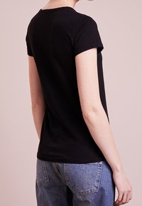 Černé tričko s krátkým rukávem vyrobené z bavlny, s kulatým výstřihem a přiléhavým střihem, spolu s modrými džínami s vysokým pasem.