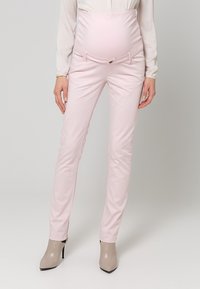 Pantaloni da maternità in rosa chiaro, design aderente con una fascia elastica per la pancia. Texture liscia, due tasche frontali e semplici decorazioni con bottoni metallici.