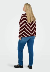 Maglione a righe bordeaux e crema con motivo a zigzag, vestibilità ampia, abbinato a jeans in denim blu e scarpe nere. Modello visto da dietro.