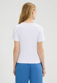 Camiseta blanca de manga corta con un escote redondo, textura suave y un diseño ajustado, combinada con pantalones holgados azules.