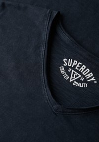 Navyblauw katoenen T-shirt met een V-hals, voorzien van een witte logotag met de tekst "Superdry" en "Crafted Quality" nabij de kraag.