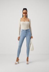 T-shirt de manga longa beje claro com decote quadrado, combinado com uns jeans skinny de cintura alta azul claro. Sandálias de salto abertas brancas.