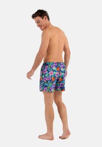 Pantaloni da nuoto con un motivo floreale blu che presenta elementi viola, arancioni e verdi. Vita elastica con un piccolo etichetta del logo sul retro.