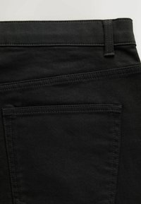 Gros plan de la poche arrière d'un jean en denim noir avec passant de ceinture visible et détails de couture sur un tissu sombre.