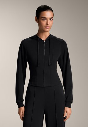Schwarze Zip-Hoodie mit taillierter Passform, langen Ärmeln und Kapuze mit Zugband. Glatte Textur mit Nahtdetails, cropped Länge.