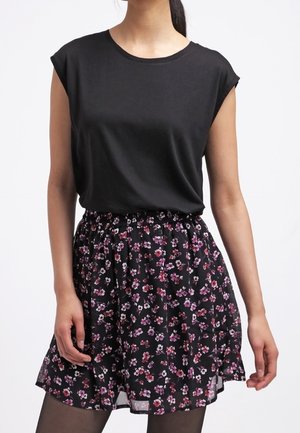Mujer con una blusa negra sin mangas metida en una falda negra con flores rosas y blancas, combinada con medias negras.