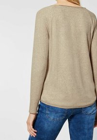 Beige långärmad topp med rundad halsringning, mjuk textur och avslappnad passform, matchad med blå jeans med subtila detaljer på bakfickorna.