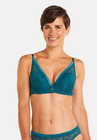 Soutien-gorge en dentelle bleu sarcelle avec un design en V, des motifs floraux, des bords festonnés, des bretelles ajustables et un accent en métal décoratif au centre.