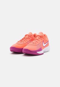 Nike treningsko med mesh-overdel i lys korall, lilla detaljer, og en hvit såle. Har en teksturert yttersåle og lissesystem.