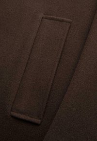 Lähikuva ruskeasta villatakkitaskusta, jossa on siisti, suorakulmainen läppä ja näkyvät saumat reunoilla.