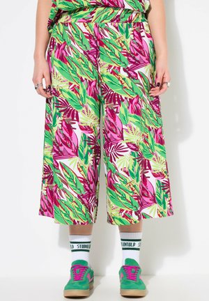Pantalones de pierna ancha, con un brillante estampado de hojas en verde y rosa, combinados con zapatillas verdes y calcetines blancos con texto verde.