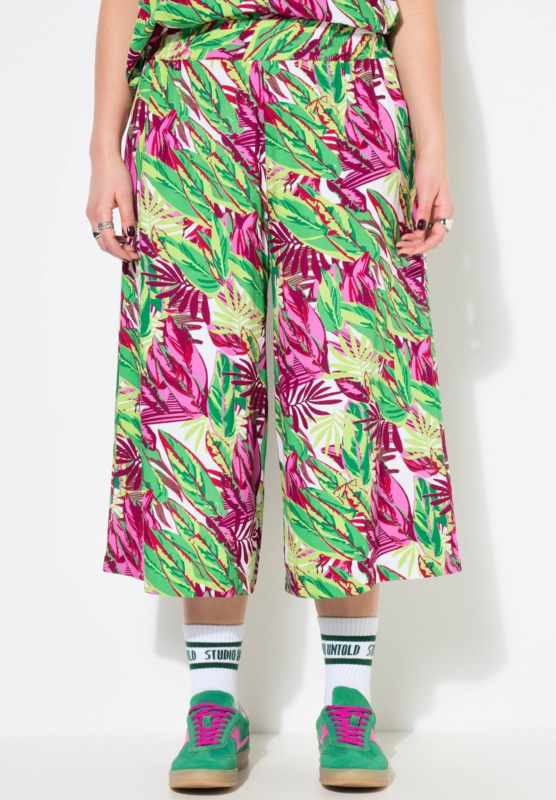 Pantalones de pierna ancha, con un brillante estampado de hojas en verde y rosa, combinados con zapatillas verdes y calcetines blancos con texto verde.