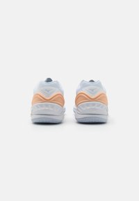 Baskets de sport blanches avec un accent orange au niveau du talon. Tige en mesh doux, semelle rembourrée et semelle en caoutchouc texturé pour l'adhérence.
