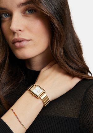 Gouden metalen horloge met een rechthoekige wijzerplaat en witte wijzerplaat. Gladde band met een gepolijste afwerking. G gedragen om een pols met een meerkleurige armband.