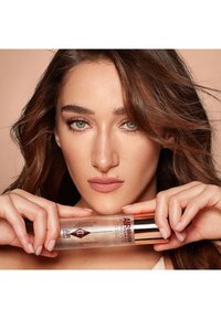 Clear spray bottle with a metallic rose gold lid, holding a setting spray. Label features bold text and a leaf design against a light background.