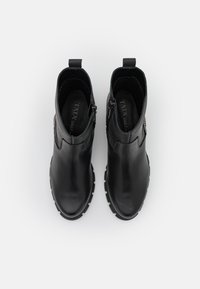 Stivali alla caviglia in pelle nera con una finitura liscia, punta rotonda, cerniere laterali e piccole suole rialzate. Presenta un accento laterale testurizzato.