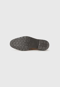 Suela de zapato de ante marrón con una parte inferior de goma negra texturizada. Presenta ranuras con patrones para mayor tracción y durabilidad.