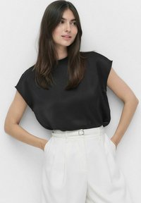 Sort satin top med korteærmer, rund halsudskæring, afslappet pasform, parret med højhælte hvide bukser og et matchende bælte.