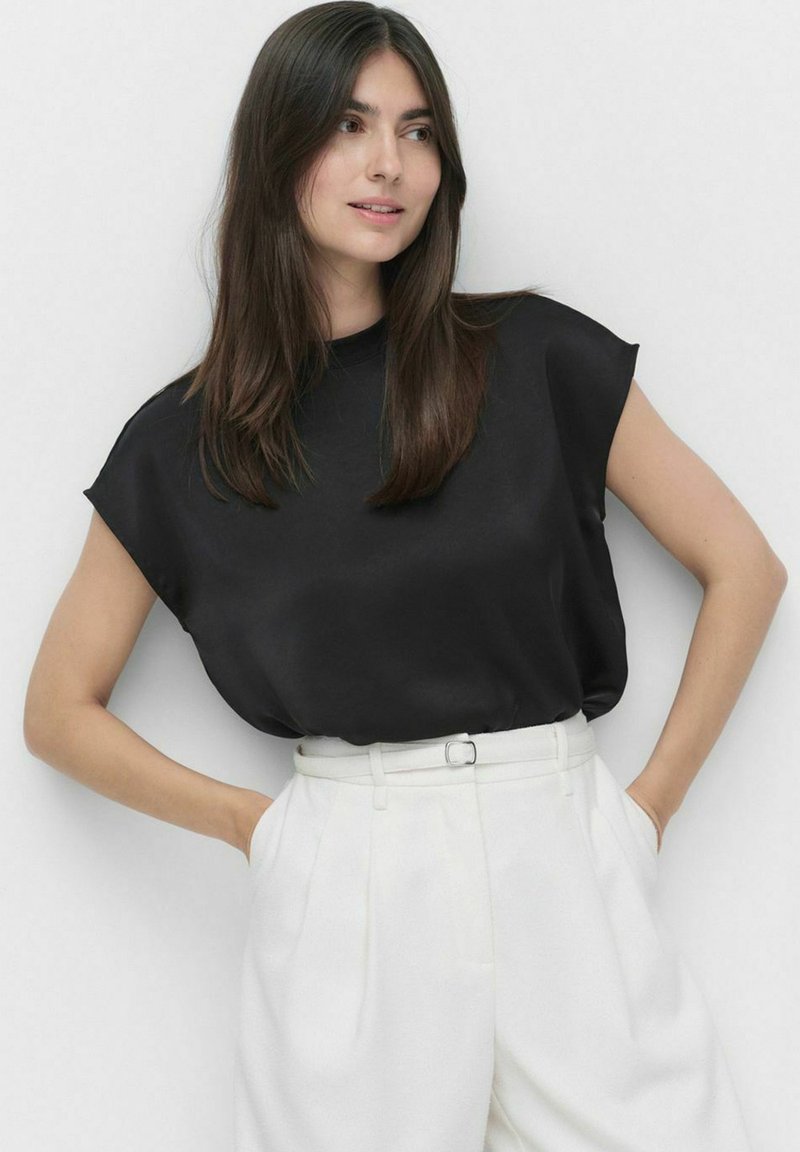 Sort satin top med korteærmer, rund halsudskæring, afslappet pasform, parret med højhælte hvide bukser og et matchende bælte.