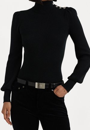 Pull noir côtelé à col roulé avec épaules bouffantes et boutons argentés sur un côté, associé à un pantalon noir et une ceinture noire avec une boucle argentée.