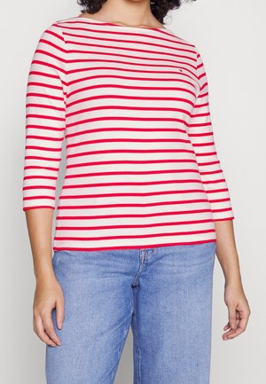 Rot-weiß gestreiftes Langarmshirt mit einem Boot-Ausschnitt und dreiviertellangen Ärmeln, aus weichem Material gefertigt und kombiniert mit hellblauen Jeans.