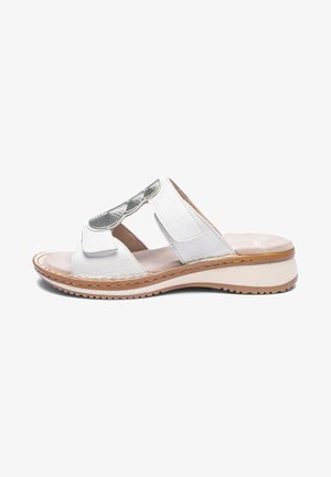White open-toe sandal with adjustable straps, silver decorative patch, beige cushioned footbed, and low wedge sole with textured outsole.