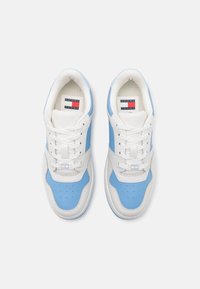 Une paire de baskets blanches et bleu clair de Tommy Jeans avec des lacets, vue de dessus sur un fond blanc.
