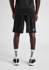 Black sports shorts with white side stripes, made of lightweight fabric, paired with white socks featuring black zigzag patterns, and black sneakers.