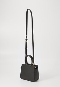 Sac à main en cuir noir avec une forme structurée, de doubles anses supérieures et une bandoulière longue amovible. Comprend des éléments en métal doré et une texture lisse.