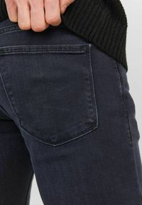 Mörka denimjeans med en sidovy av en bakficka, med en solid struktur och minimala sömnadsdetaljer, bärs med en svart ribbad tröja.