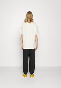 T-shirt blanc à manches courtes associé à un pantalon de jogging noir et des baskets jaunes. Le t-shirt a une coupe décontractée ; le pantalon de jogging présente des poignets élastiques.