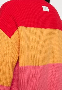 Strickpullover mit horizontalen Streifen in Rot, Orange, Gelb und Pink. Hat eine strukturierte Oberfläche und ein kleines Logo-Tag auf der Rückseite.