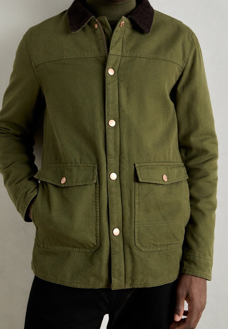 Veste vert olive avec un col en velours côtelé marron, dotée de boutons en cuivre et de deux poches avant, fabriquée dans un tissu durable.