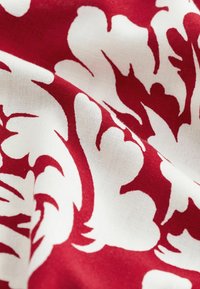 Tissu rouge avec un motif floral abstrait blanc et des plis de texture visibles.