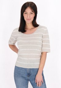 Beige kötött felső fehér vízszintes csíkokkal, kerek nyakkivágással és rövid ujjakkal, kék farmernadrággal párosítva. Egyszerű, textúrált dizájn.