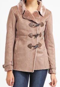 Beige faux suede frakke med en blød pelskrave, der har hjerteformede knapper og en tætsiddende talje. Lange ærmer med spænde detaljer.