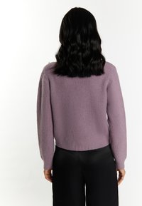 Paarse gebreide trui met een textuur en een cropped fit, afgewerkt met een ribbelrand. Heeft een unieke accent op de schouder. Gecombineerd met aansluitende zwarte broek.
