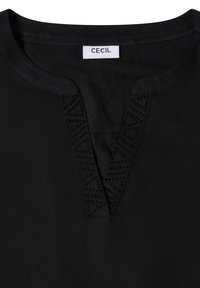 Blusa negra con escote en V, detalles texturizados y costuras decorativas. Confeccionada en tela suave y corte holgado.