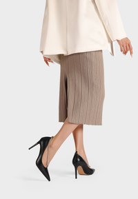 Scarpe nere con tacco alto, punta affusolata e cinturini alla caviglia. Le scarpe presentano una finitura in pelle liscia e un sottile dettaglio in gemma.