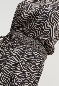 Tkanina s potiskem zebry v černé a béžové barvě je doplněna texturovaným pleteným elastickým páskem s šňůrkou, což vytváří design s uvolněným střihem.