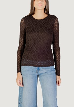 Top lungo a maniche nere in pizzo con motivo a zigzag e scollo rotondo, abbinato a jeans a gamba larga in denim blu chiaro con orli grezzi.
