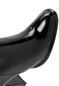 Botín negro de charol hasta el tobillo con punta afilada, tacón angular y textura suave y brillante. Presenta líneas limpias y un detalle mínimo.