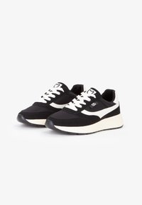Zapatillas en blanco y negro con un diseño de malla y gamuza, punta redonda, suela media blanca gruesa, una franja contrastante y cordones prominentes.