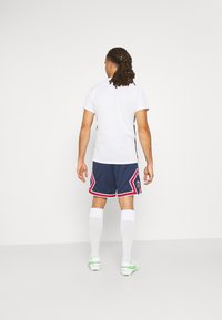 Vit kortärmad skjorta med svarta sidokanter, tillsammans med blå shorts med röd och vit trim, vita strumpor och gröna fotbollsskor.