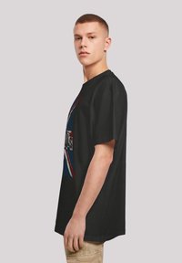 Black cotton t-shirt with a loose fit, featuring a graphic design in red, white, and blue. Crew neck and short sleeves.