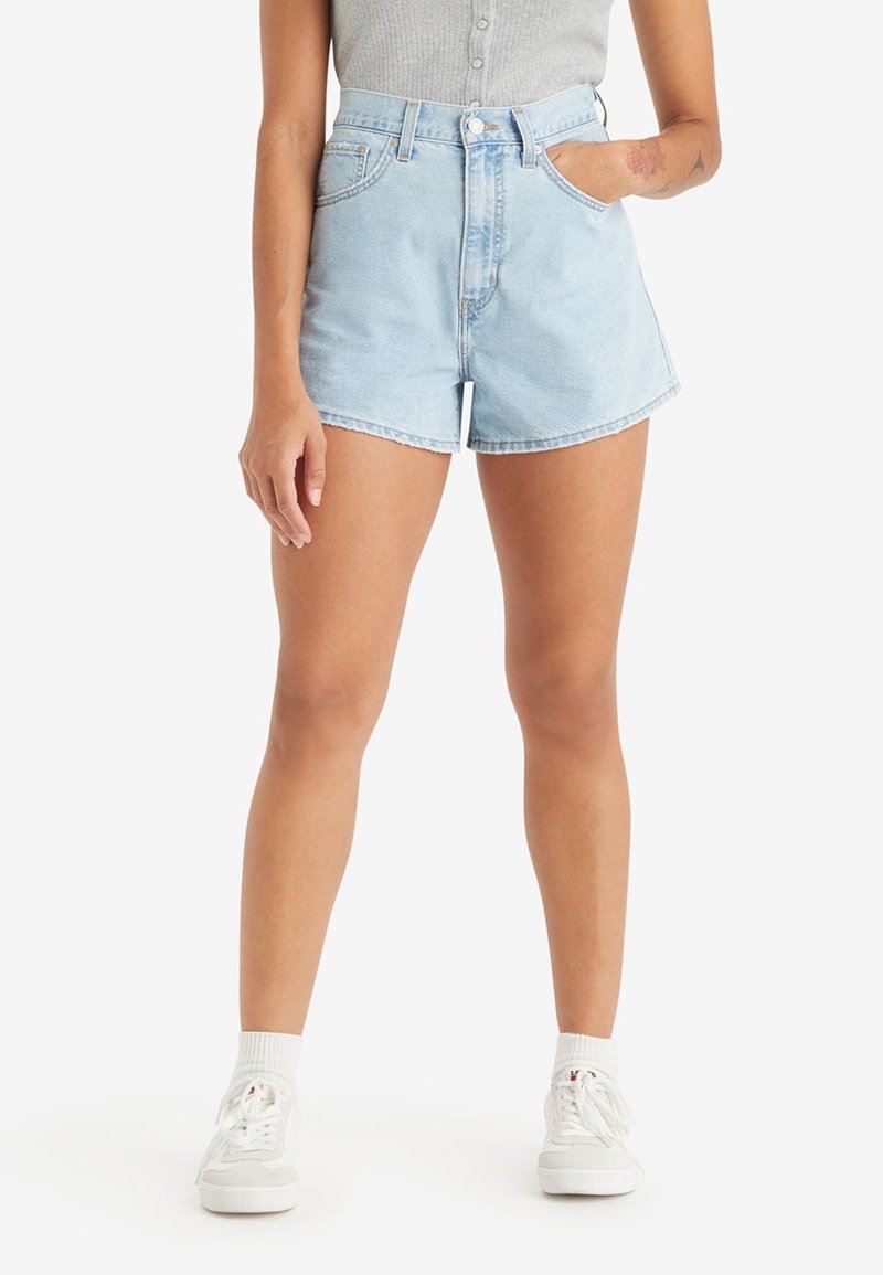 Light blue denim shorts with a high waist, featuring a button closure, front pockets, and a slightly curved hem. Paired with white sneakers.