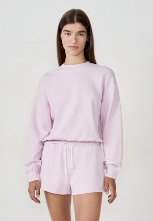 Lichtroze sweatshirt met lange mouwen en een ronde hals, gecombineerd met bijpassende korte broek met een elastische tailleband en trekkoord.