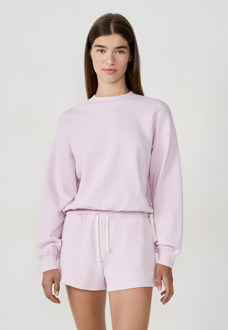 Jasnoróżowy sweatshirt z długimi rękawami i okrągłym dekoltem, w połączeniu z dopasowanymi szortami z elastycznym pasem i sznurkiem.